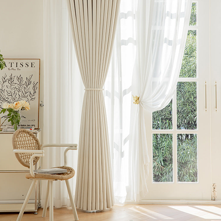 Beige curtains with sheer white panels in a room with a chair and decorative elements.